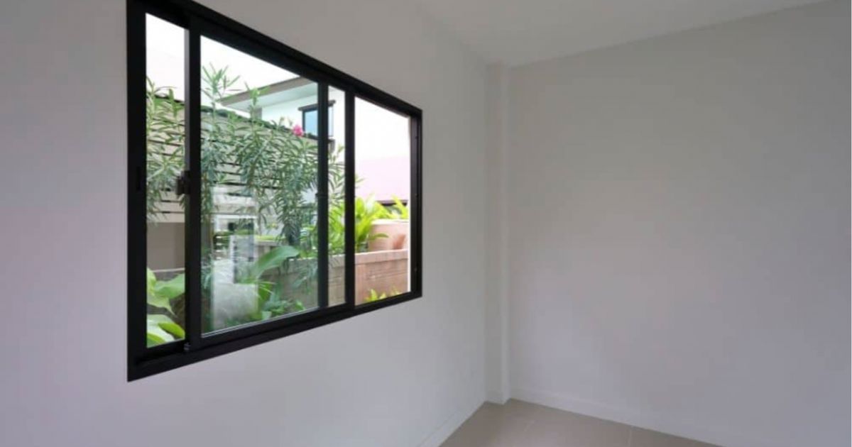 Een kamer met witte muren en een schuifraam met zwarte kozijnen. Het raam staat open en in de tuin staan enkele planten