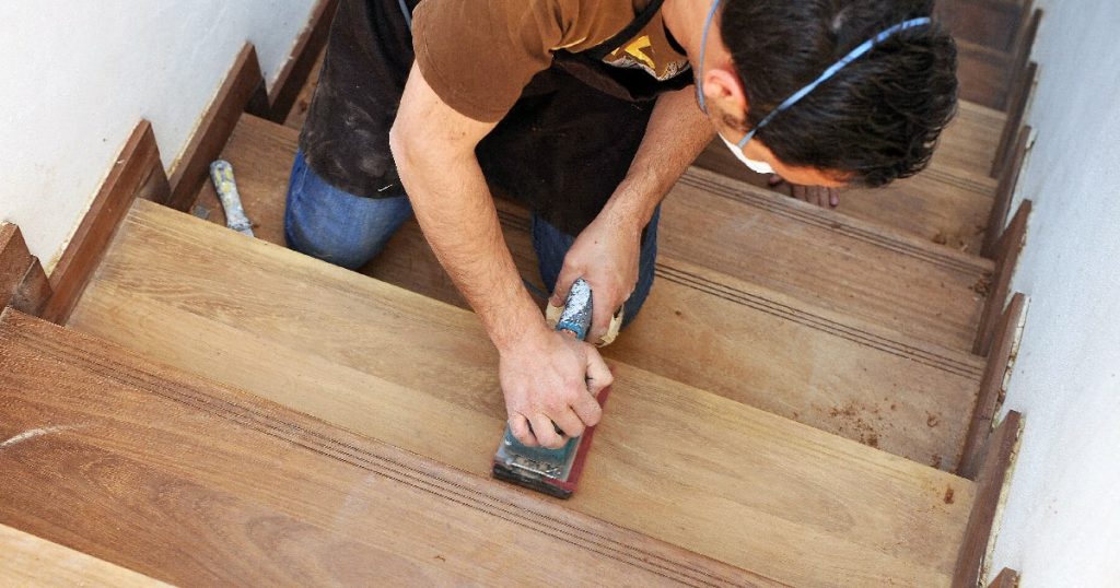 Een man gebruikt een schuurblok om een houten trap te schuren.