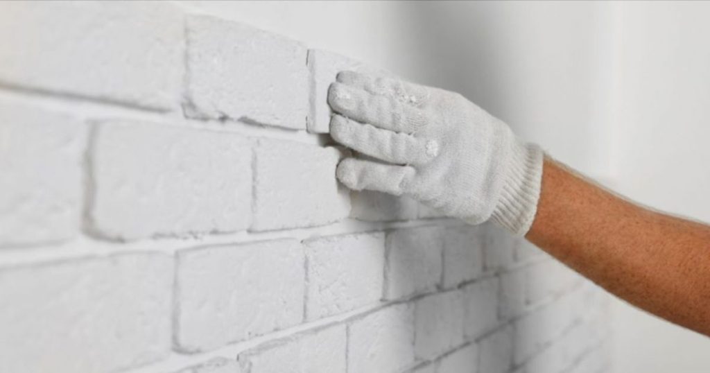 Een vakman heeft een witte handschoen aan en plaatst steenstrips op een witte muur van gevelpleister