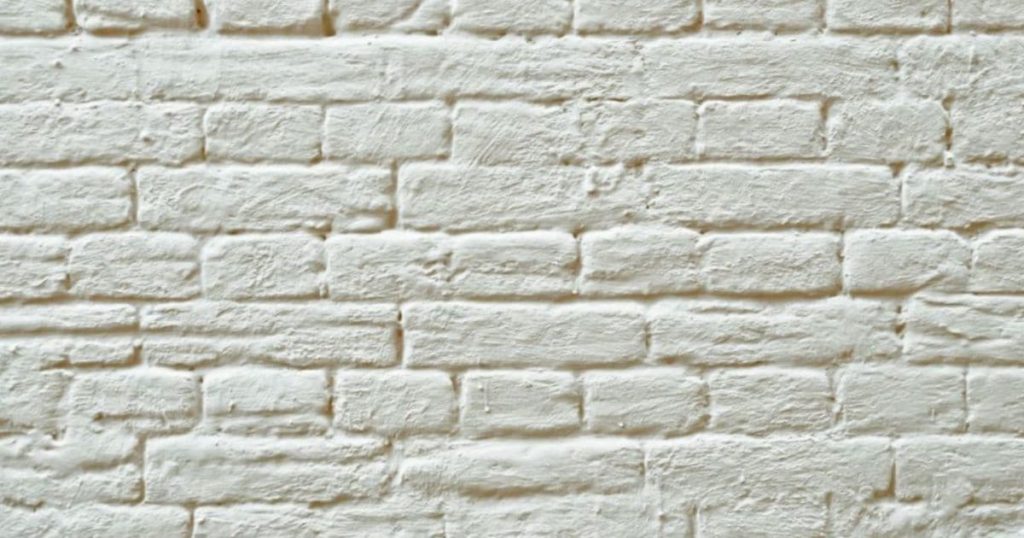 Een witte gevel met sierpleister en een baksteenmotief