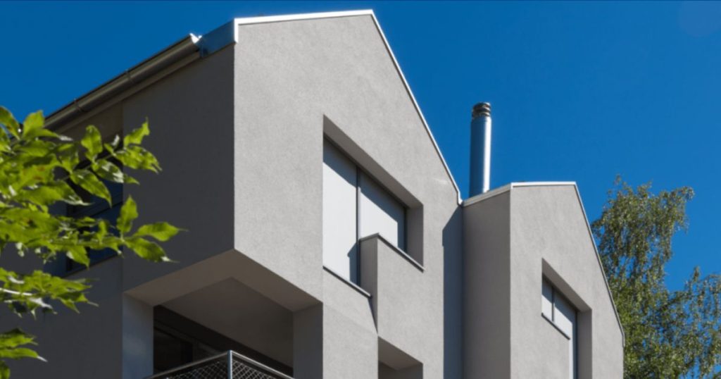 Een groot vrijstaand modern huis heeft een gevel van sierpleister met een grijze betonlook