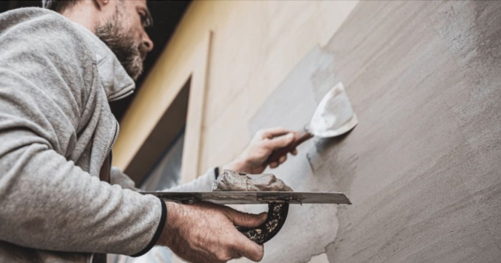 Een stukadoor brengt sierpleister aan op een gevel met een spatel