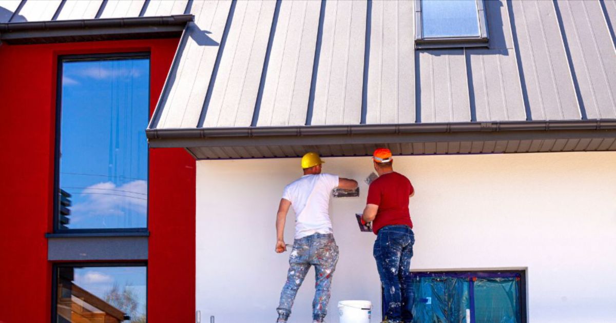 Twee gevelwerkers zijn de buitenmuren van een huis aan het stucen.  