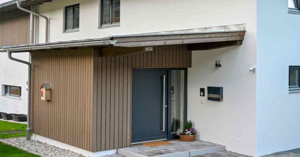 Woning met wit pleisterwerk en verticale houten gevelbekleding rond de overkapte entree met moderne voordeur.