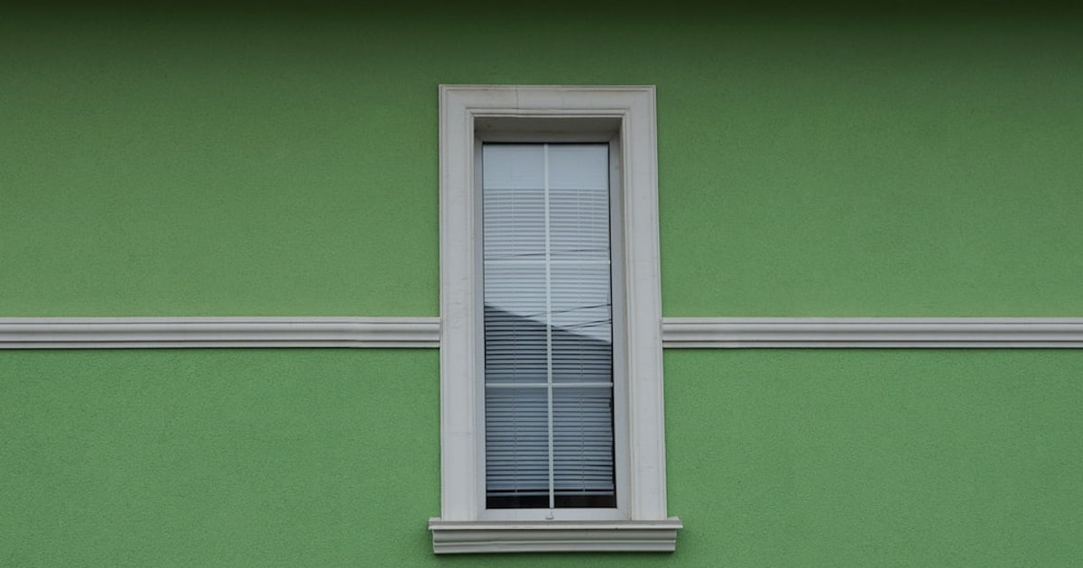Een opvallende groene gevel gemaakt van sierpleister. In het midden is een raamkozijn zichtbaar.