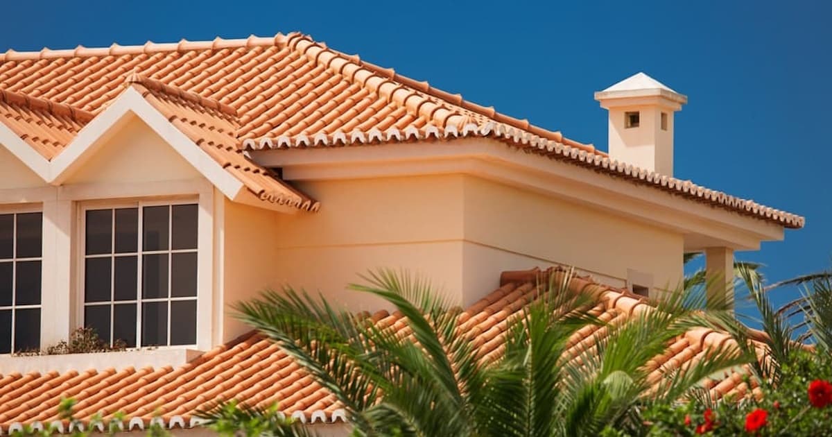 Een gebouw met een oranje sierpleister gevel. Op de voorgrond zien we een palmboom, op de achtergrond een strakblauwe lucht.