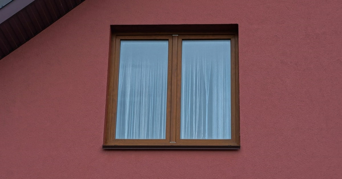 Een close-up van een houten kozijn in een rode gevel gemaakt van sierpleister. Het kozijn is bruin.