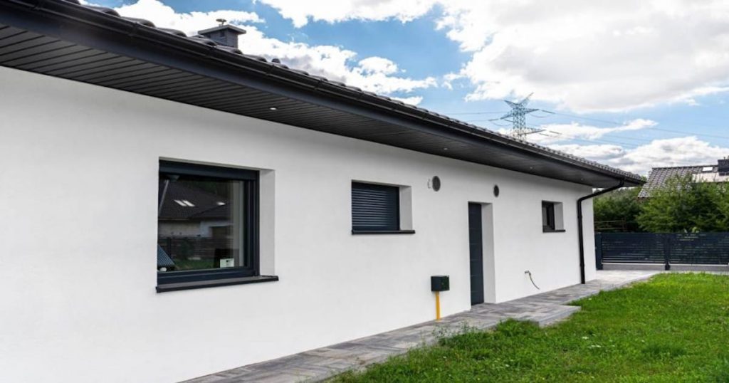 Een frisse, witte gevel gemaakt van sierpleister. Het wit contrasteert mooi met het groene gazon en de blauwe lucht.