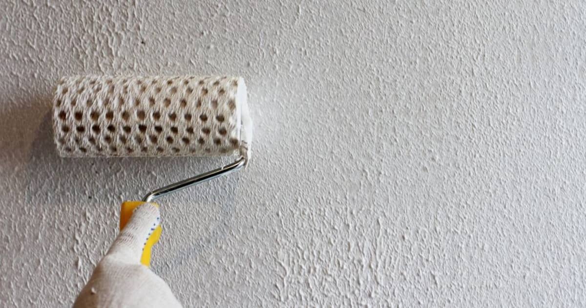 Met een speciale roller zorgt een gevelspecialist ervoor dat een structuur in de sierpleister gevel zichtbaar is.