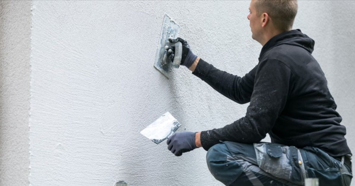 Een gevelspecialist is de muren van een huis aan het bepleisteren met sierpleister.