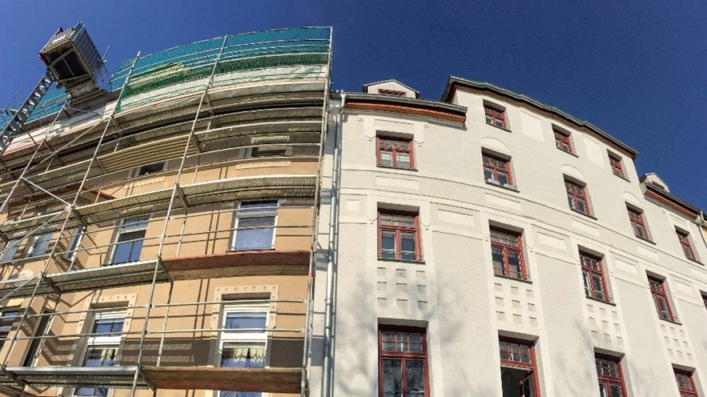 De voor en na van een gevelrenovatie. De sierpleister heeft op de rechterhelft een fris laagje lichte verf gekregen. Links is de oude, vergeelde kleur zichtbaar.