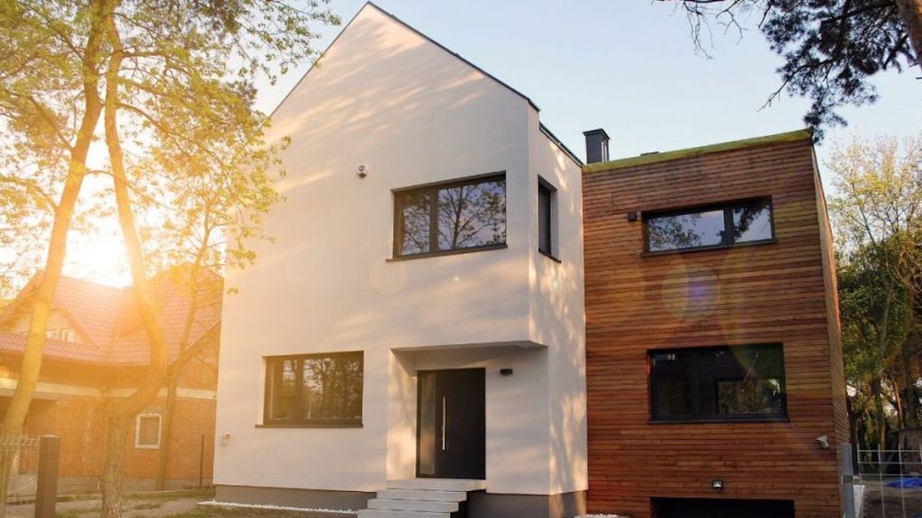 Een moderne woning met een strakke, witte sierpleister op de gevel. De sierpleister wordt gecombineerd met houten elementen en donkere kozijnen. 