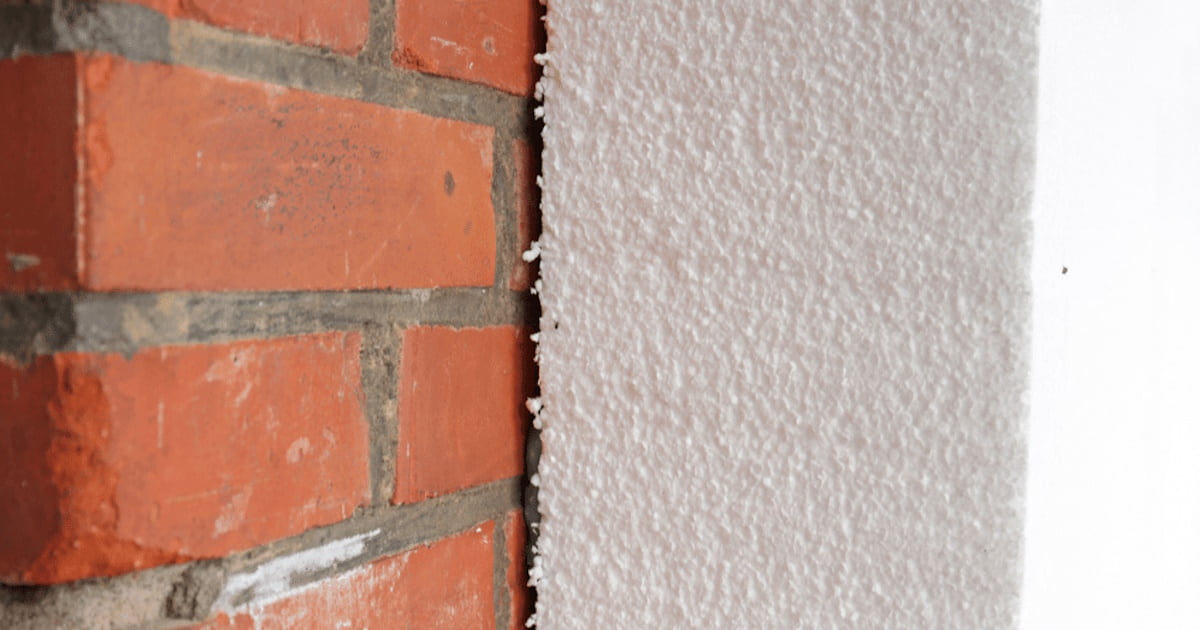 Een close-up van een EPS isolatieplaat die tegen een rode bakstenen gevel wordt geplaatst.