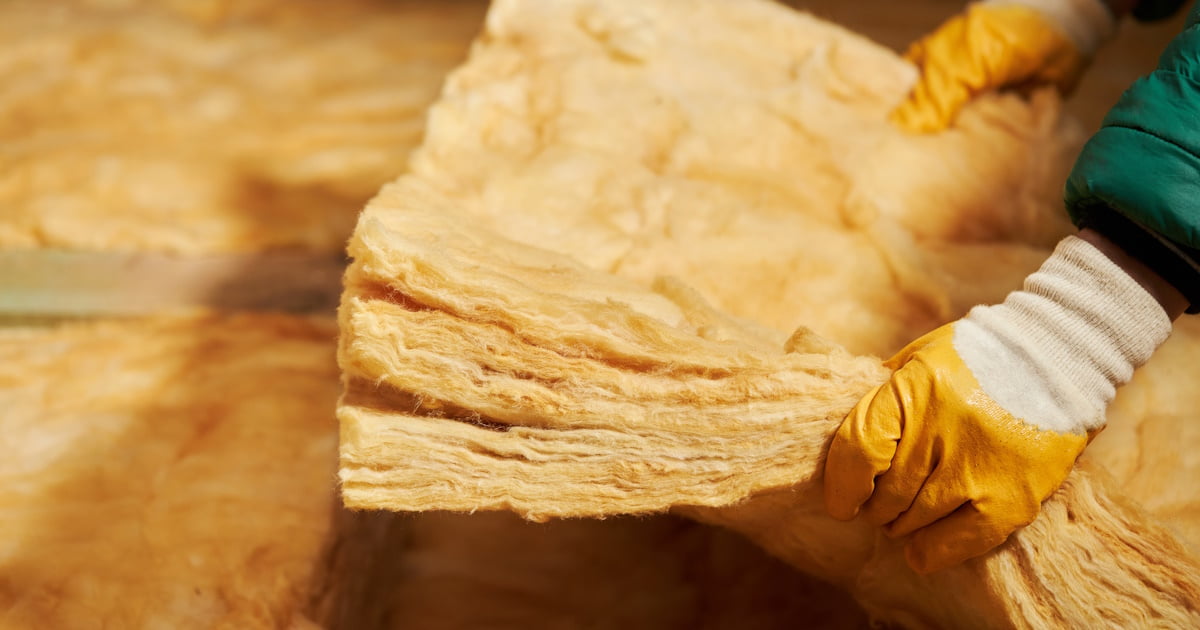 Een persoon draagt handschoenen om zich te beschermen tegen de irriterende vezels van een strook glaswol