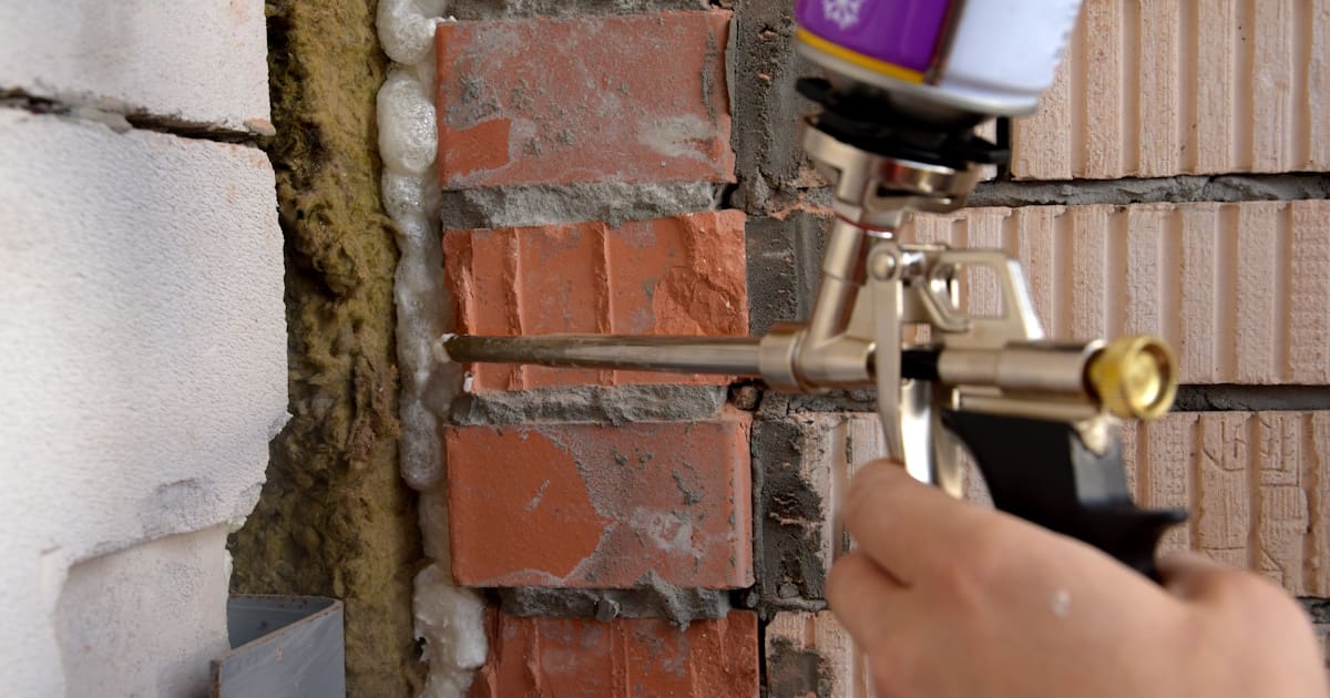 Een isolatiespecialist brengt isolatieschuim aan in de ruimte achter een muur. Naast de laag schuim is een laag minerale wol zichtbaar