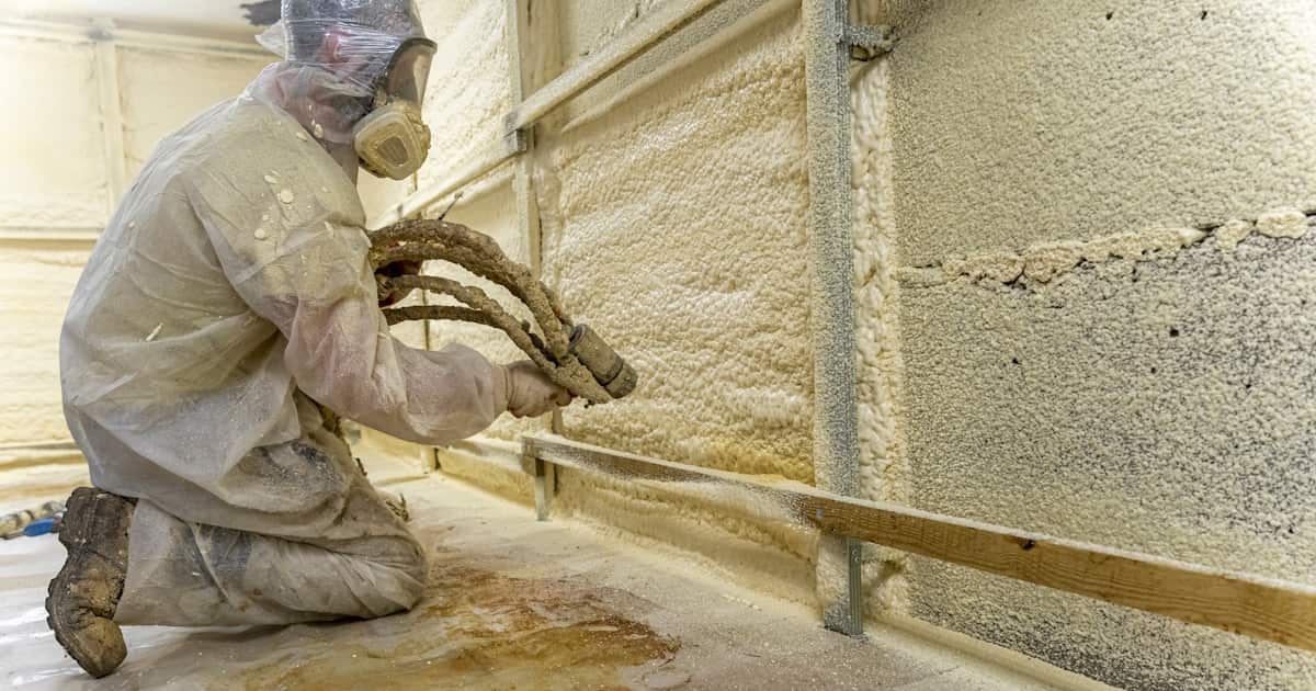 Een isolatiespecialist brengt isolatieschuim aan met een spuitpistool. De expert draagt beschermende kleding
