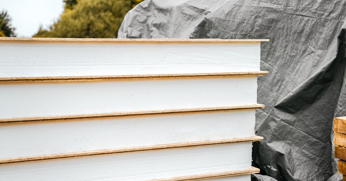 Een stapel isolatieplaten met telkens een houten plaat ertussen, op de achtergrond een donker zeil