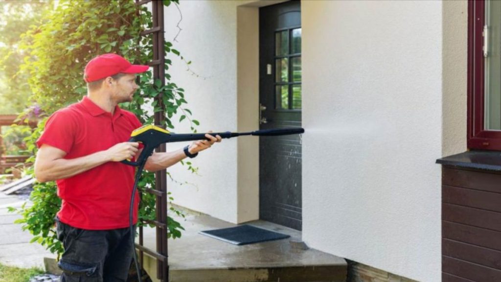 Een gevelspecialist onderhoudt de sierpleister gevel door deze met een sproeier schoont te spoelen.