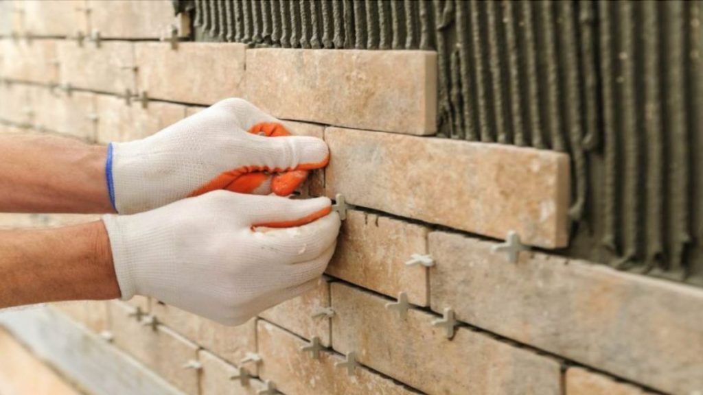 Een gevelspecialist is bezig met het bevestigen van beige steenstrips op een muur