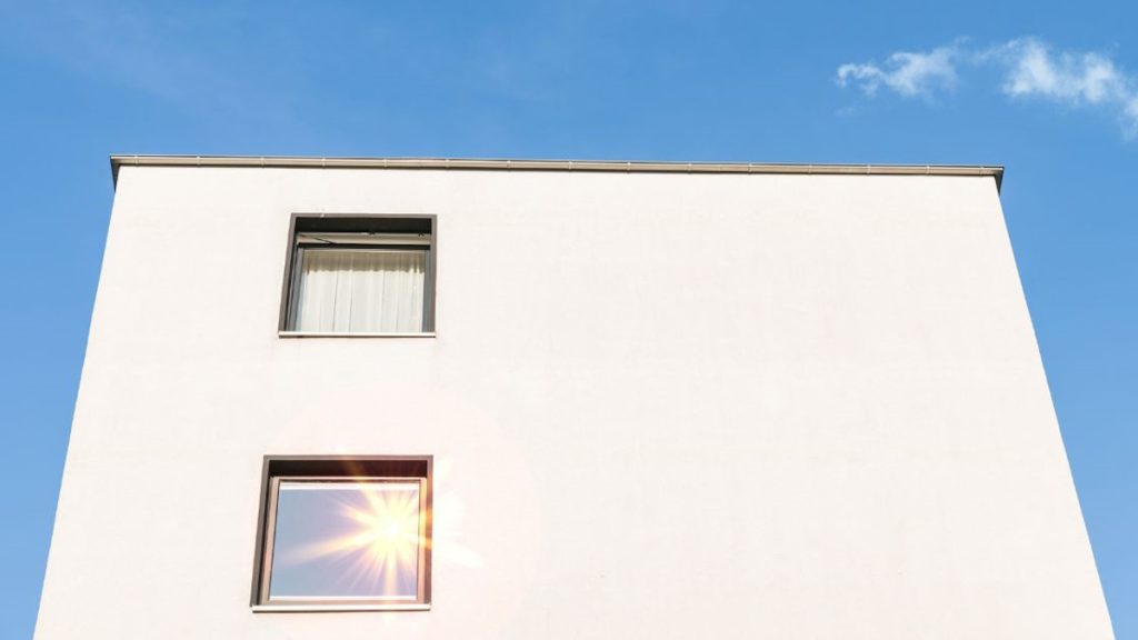 Gladde kalkpleister afwerking steekt af tegen blauwe hemel. De gevel heeft een moderne uitstraling.