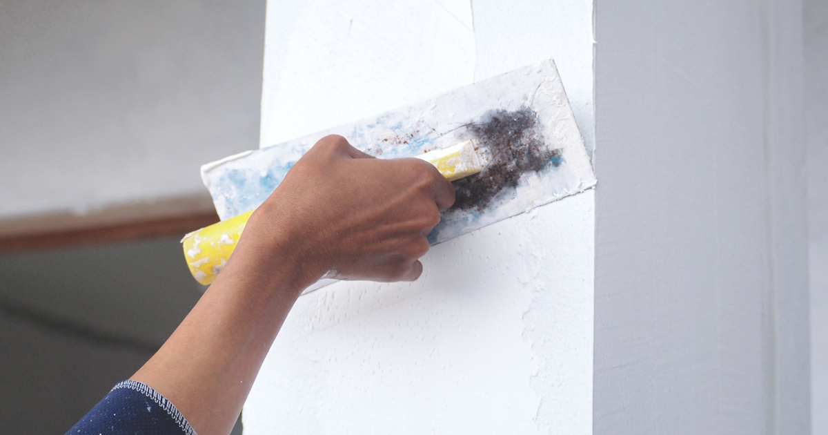 Een stucadoor stuct een buitenmuur.