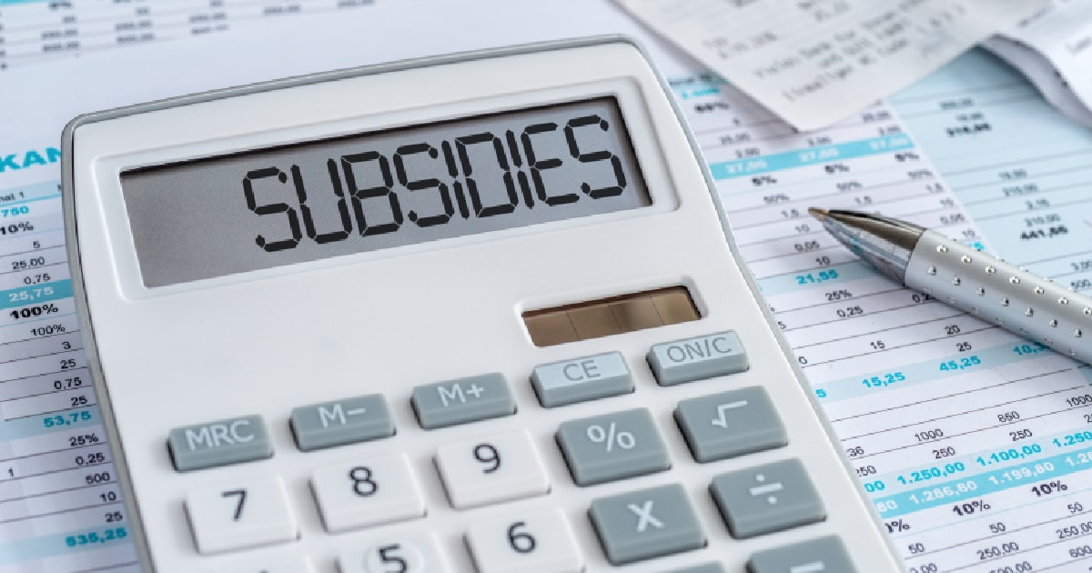 Een rekenmachine met de tekst 'subsidies', op de achtergrond facturen, rekeningetjes en een pen.
