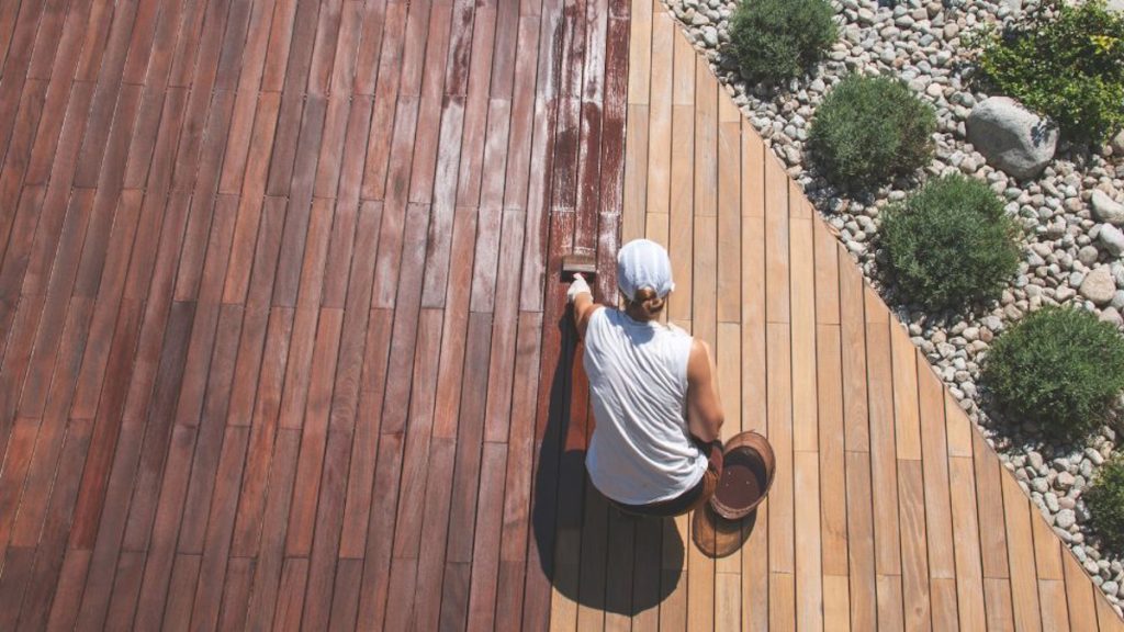 Een houten oppervlak wordt behandeld met een laag beits. De schilder gebruikt er een blokkwast voor.