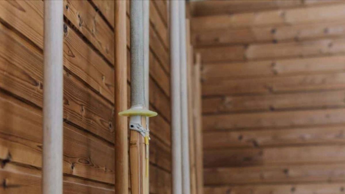 Close-up van een houten wand met zichtbare thermowood gevelpanelen en leidingen.