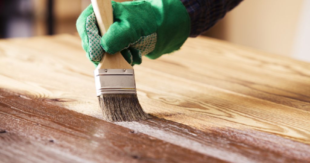 Een schilder beitst een houten oppervlak met een kwast