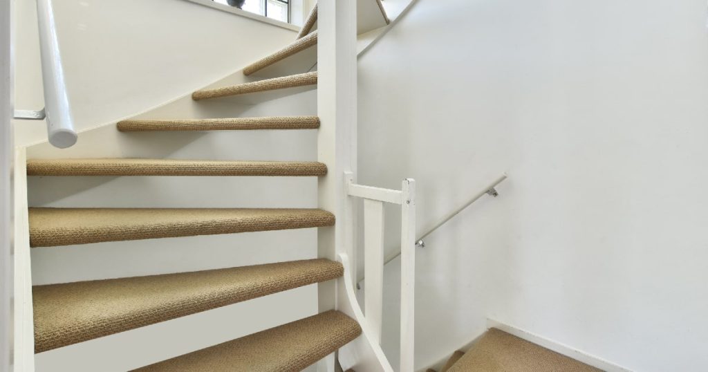 Een tweekwart trap met open constructie uit wit hout en met tapijt beklede traptreden.