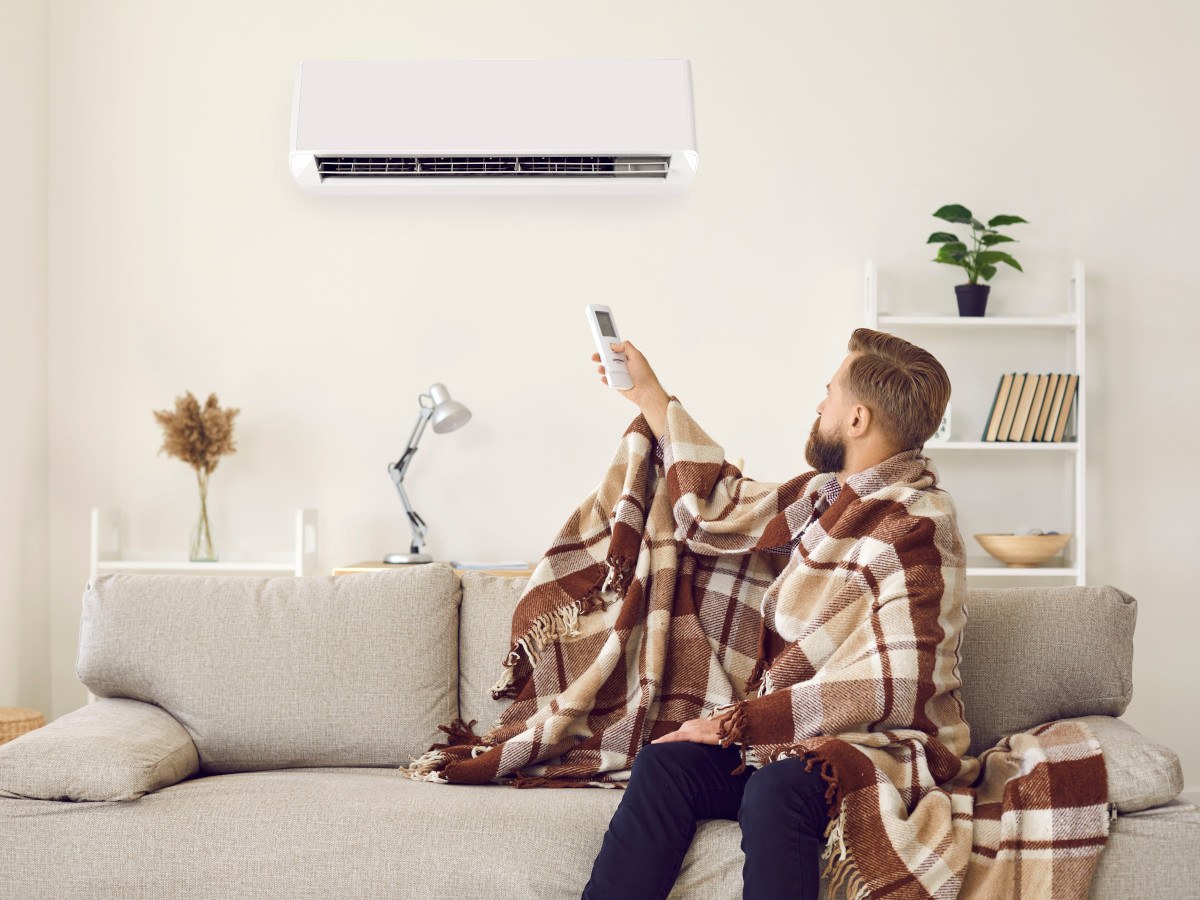man met deken om zich heen op een grijze bank die de airco aanzet voor verwarming