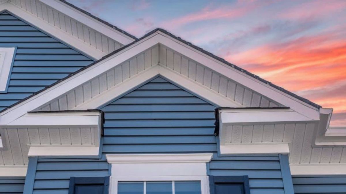 Close-up van een woning met blauwe vezelcement gevelbekleding en witte dakranden, bij zonsondergang.
