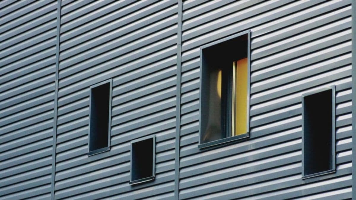 Moderne gevel met antracietgrijze vezelcement gevelbekleding in horizontale profielen met smalle rechthoekige ramen.