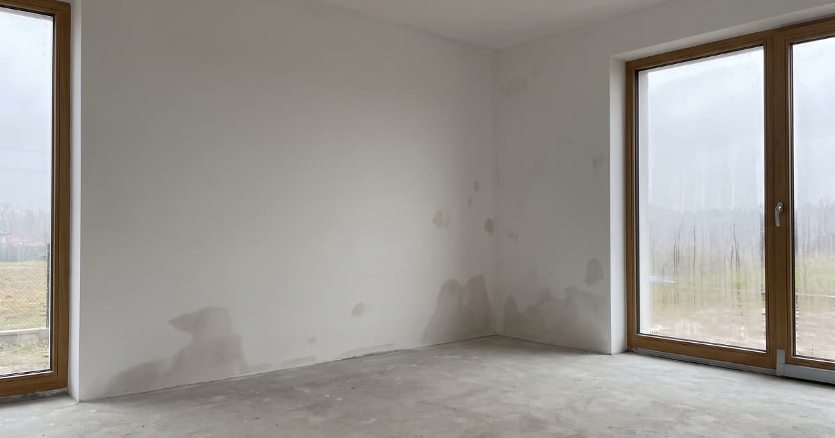Vochtplekken zijn zichtbaar onderaan de muren van een onafgewerkte nieuwbouwwoning met condens op de ramen.