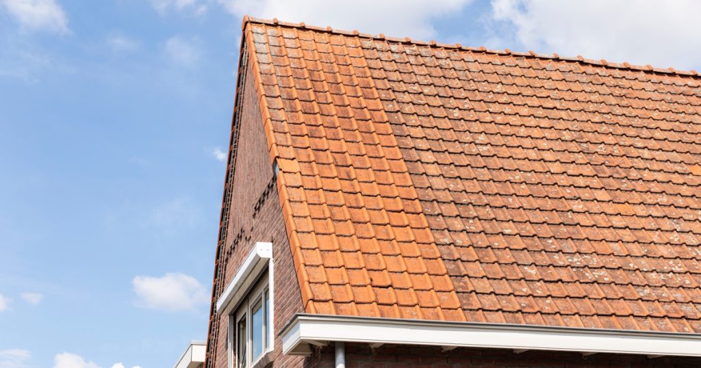 De gevel van een vrijstaande woning. Op het dak liggen rode dakpannen waarvan een deel is gereinigd.