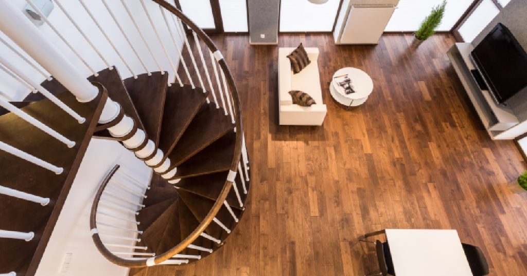Een wenteltrap uit donker hout. De trap staat in een minimalistische woning met een bruine, houten vloer.