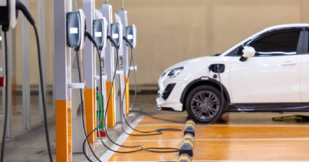 De oranje parkeerplaatsen zijn voorzien van laadpalen. Op de achtergrond een witte elektrische auto.