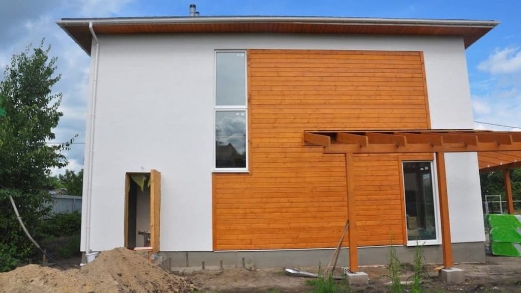 Een moderne woning met een gevel van witte sierpleister gevel en hout tegen een blauwe lucht. 