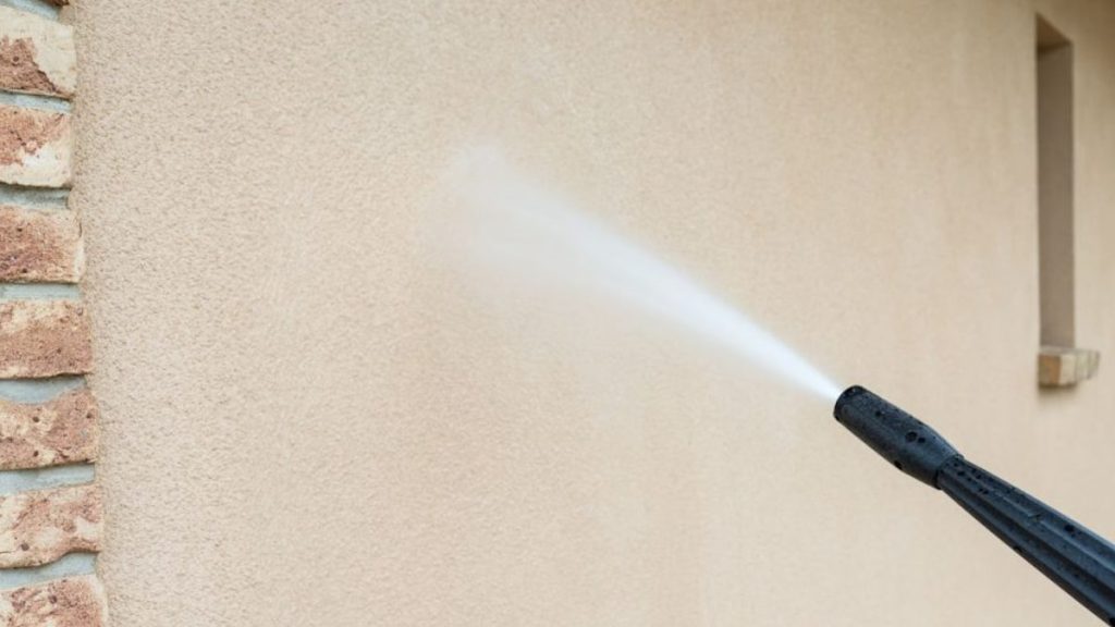 Een beige sierpleister gevel wordt schoongemaakt met een hogedrukreiniger. 