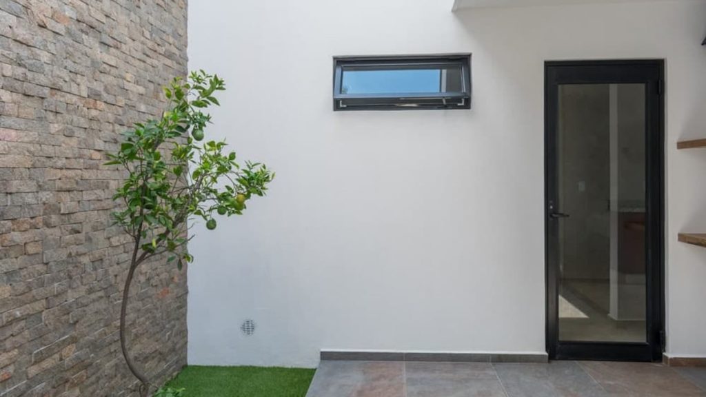 Een woning met een gevel van witte sierpleister en een bakstenen muur met een fruitboom op de voorgrond. 