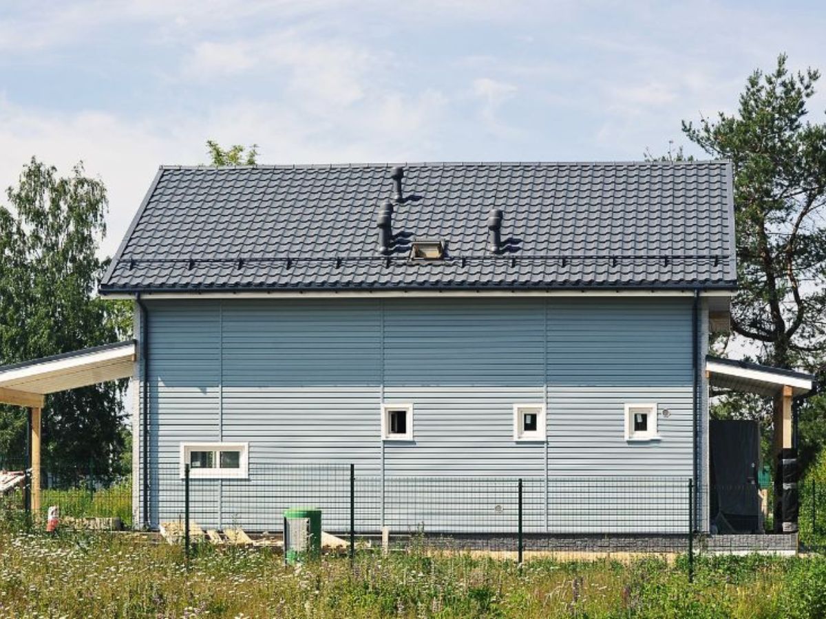 Woning met blauwe sandwichpanelen gevelbekleding en een grijs dak, omgeven door natuur.