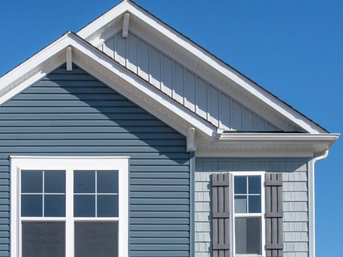 Woning met blauwe en grijze kunststof gevelbekleding in verschillende panelen en klassieke ramen met luiken.