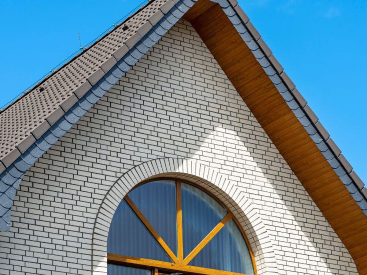 Woning met kunststof gevelbekleding in baksteenlook, voorzien van een groot rondboograam en grijs pannendak.