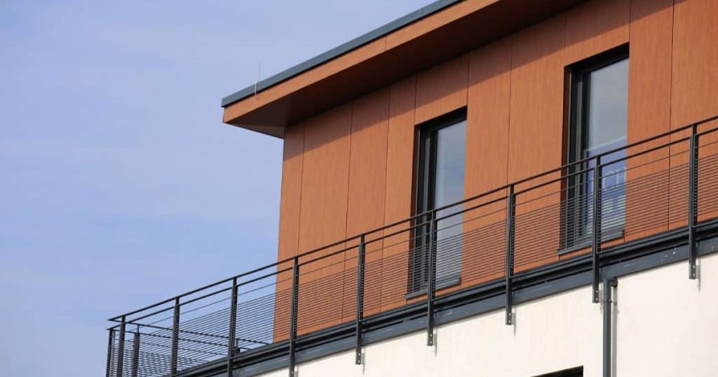 PVC-gevelbekleding in houtlook op moderne woning met zwarte kozijnen en balkonleuning.