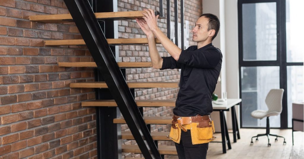 Een jonge man in een zwart hemd met een gele toolbelt houdt zich bezig met het wrappen van een trap met trapboom in het kader van een traprenovatie.