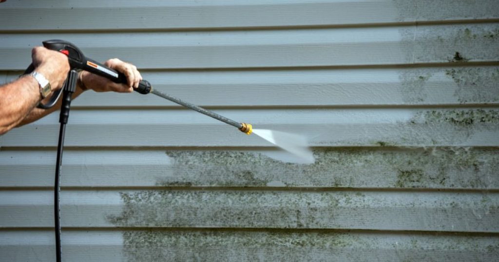 Een gevel waarop groene aanslag te zien is wordt gereinigd met een hogedrukreiniger.
