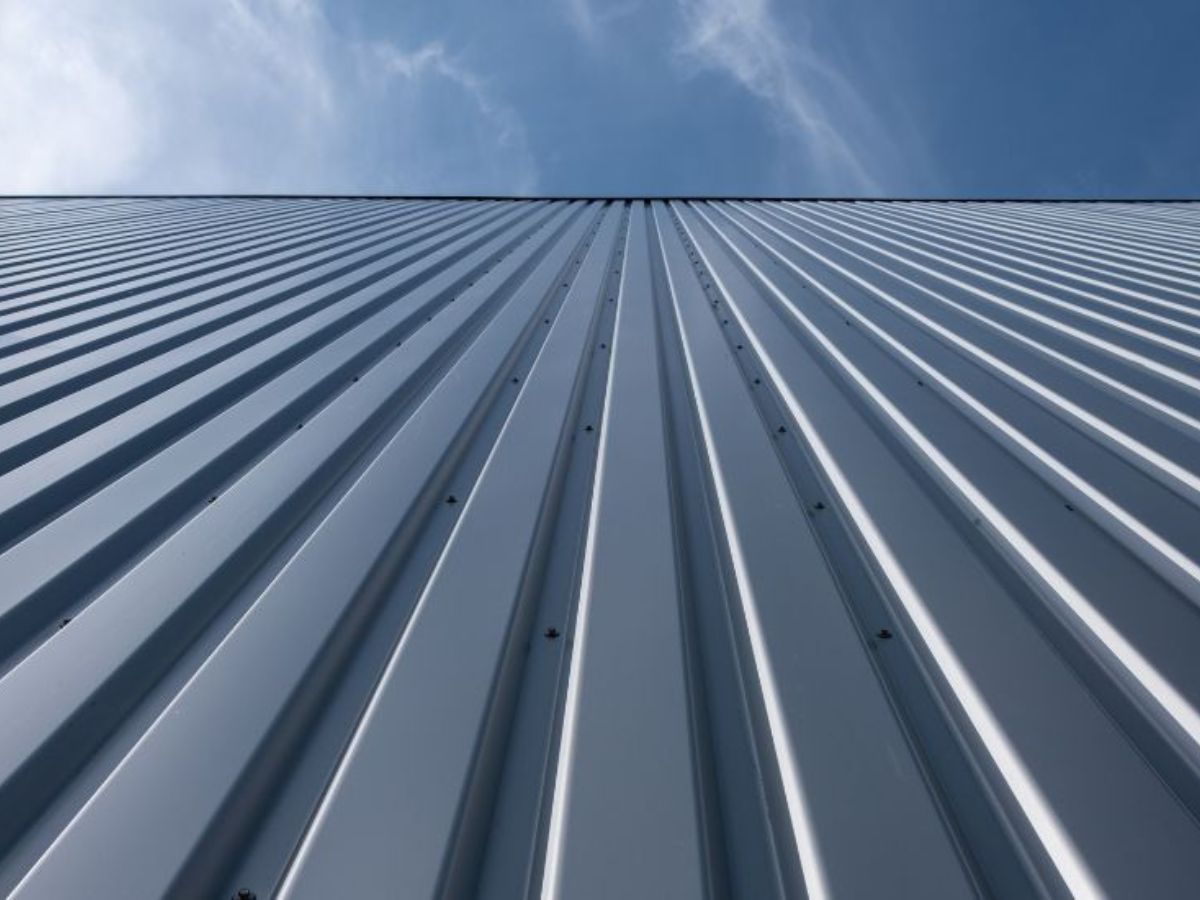 Foto van een metalen gevelbekleding van een gebouw, gezien vanuit de onderkant, met horizontale golvende lijnen en een heldere blauwe lucht op de achtergrond.