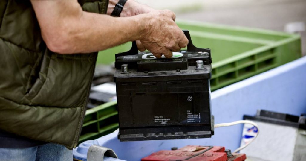 Een man met een groene bodywarmer recycleert een zwarte batterij.